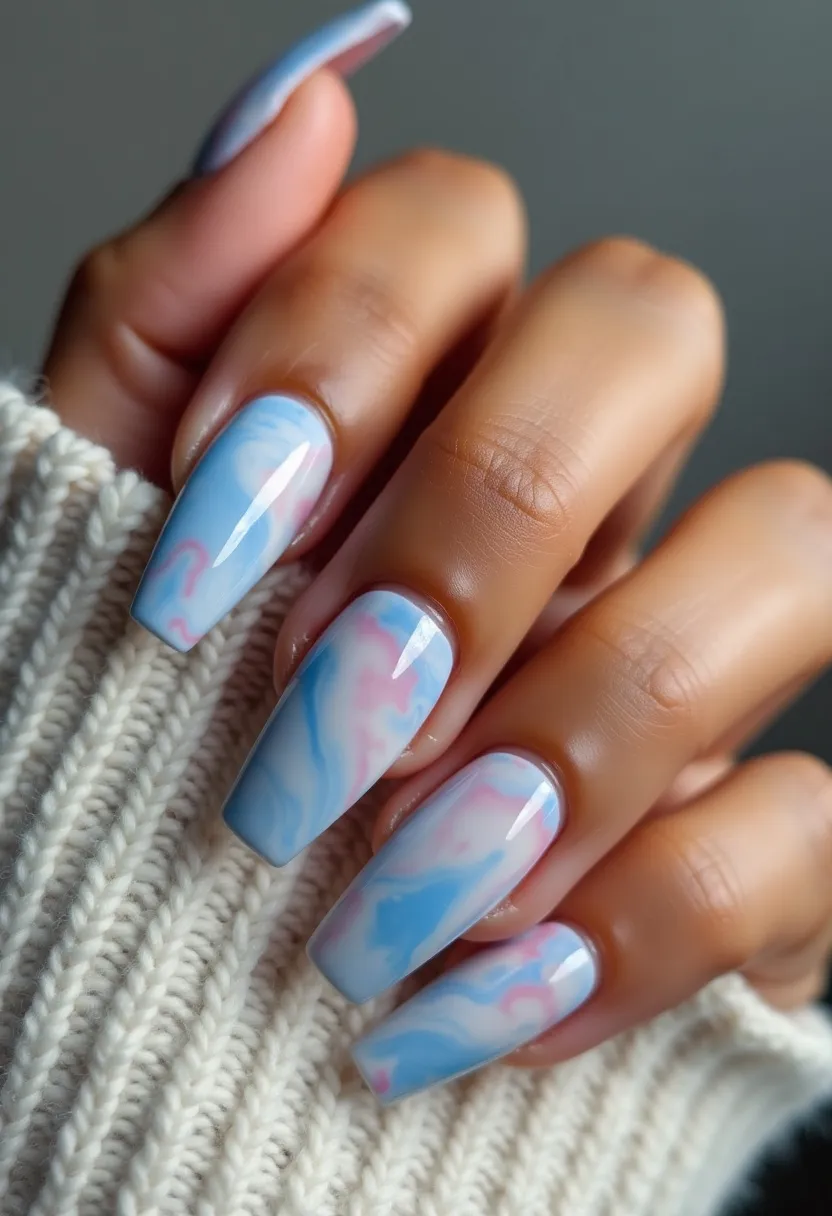 The nail design features a soft and elegant color palette dominated by pastel blues and pinks, blended seamlessly in a marbled pattern. The nails are long and shaped into a square form with rounded edges, providing a balanced and sophisticated look. The intricate marbled pattern showcases delicate swirls of blue, pink, and white, creating a dreamy and cloud-like effect. The nails appear to be treated with either gel or acrylic, providing a glossy and smooth finish that enhances the overall appearance of the design. This nail art could be ideal for various occasions, including spring or summer-themed events, due to its soft and airy feel.