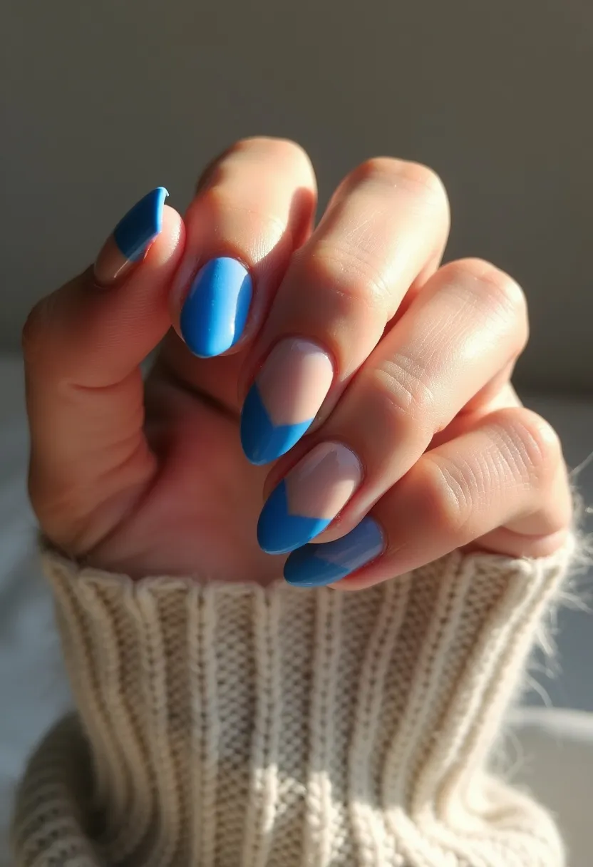 The nail design features a vibrant color palette dominated by a bold blue shade and a neutral base color. The nails are shaped in a medium-length almond fashion, giving them a sleek and elegant look. The design includes a half-moon blue tip on some of the nails, creating a geometric and modern aesthetic. This appears to be a gel manicure due to the glossy finish and precise application. There are no seasonal themes or special occasion markers in the design, but the striking blue and clean lines make it suitable for both casual and formal settings.