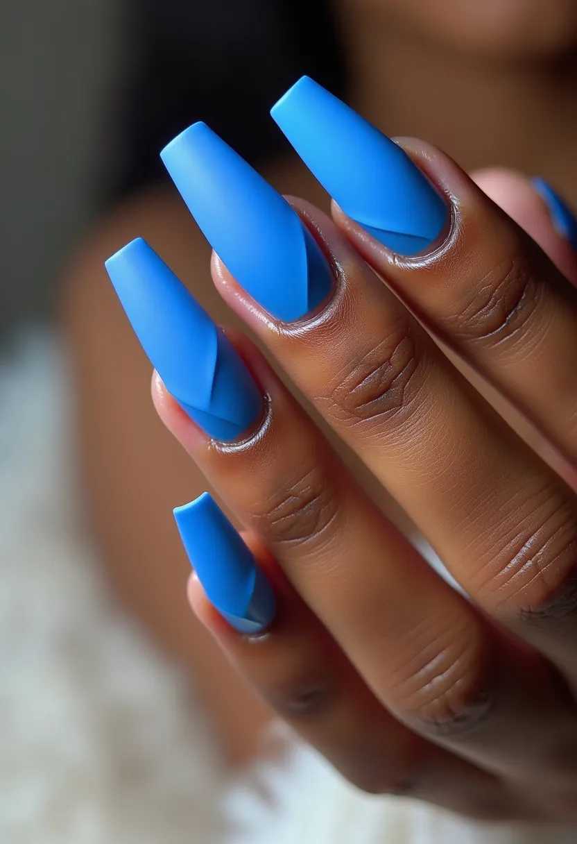 The nail design features a striking matte blue color palette applied to long, coffin-shaped nails. The nails exhibit a sleek, angular pattern, with each nail displaying an abstract geometric design that enhances the modern aesthetic. The rich blue hue and matte finish suggest a gel treatment, providing a smooth and sophisticated look. The design appears versatile, suitable for various occasions, but its cool tone and clean lines could be particularly fitting for a winter or contemporary-themed event. The overall appearance is both bold and elegant, making a stylish statement.