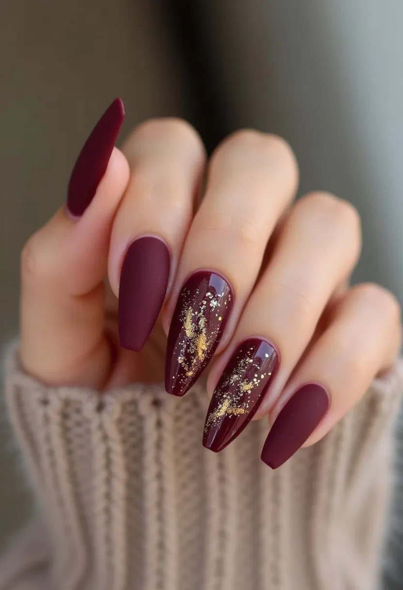 The nail design showcases a stylish, elongated stiletto shape with a sophisticated burgundy color palette. The nails employ a mix of matte and glossy finishes, creating an elegant contrast. Distinctive details include gold foil accents on the middle and ring fingers, adding a touch of glamour to the classic color scheme. The nails appear to be done using a gel or acrylic technique, providing a durable and glossy finish that is ideal for the festive season or special occasions. The golden foil detailing enhances the overall luxe feel, making it suitable for events or seasonal celebrations.