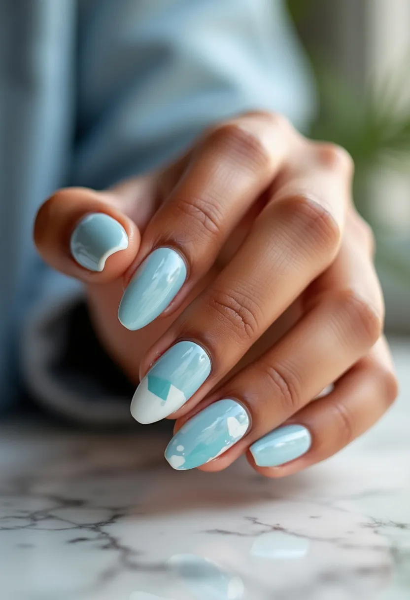 The nail design features an almond shape and uses a light blue color palette. The treatment appears to employ a gel application, giving the nails a glossy finish. Each nail showcases unique, intricate patterns, with some having diagonal white tips and a geometric pattern blending different shades of blue and white. This design has a fresh, clean look, suitable for a winter season theme or perhaps a special event like a winter wedding. The subtle blending of colors and precise execution of geometric shapes highlights the sophistication and attention to detail in the nail art.