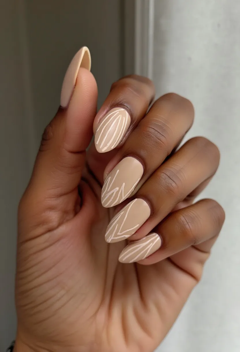 This nail design features a delicate and elegant look with a neutral color palette primarily consisting of beige hues. The nails are almond-shaped, providing a sophisticated and elongated appearance. The design includes intricate white line patterns on a few nails, adding a subtle yet eye-catching detail. This could be done using gel polish, known for its glossy finish and durability. Given the neutral tones and understated decoration, this style is versatile, suitable for both everyday wear and special occasions. The overall look is minimalist and refined, making it appropriate for various seasons, especially spring or summer, when lighter colors are favored.