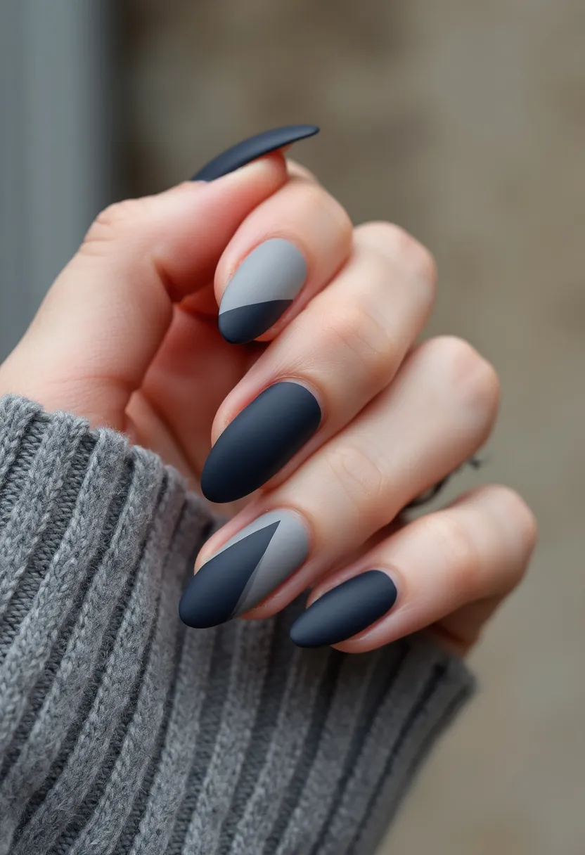 The nail design features a modern and sophisticated color palette dominated by shades of gray and black, predominantly in a matte finish. The nails are shaped into a refined almond form, adding a stylish and elegant touch. Intricate geometric patterns are the highlight of this design, with diagonal and triangular sections creating a dynamic and eye-catching effect. The black and gray hues blend seamlessly, giving the nails a sleek and contemporary appearance, likely mistaking them as treated with gel for their smooth and polished finish. This design is versatile and can be associated with a variety of occasions, including formal events or the fall/winter season, given its muted and classy color scheme.