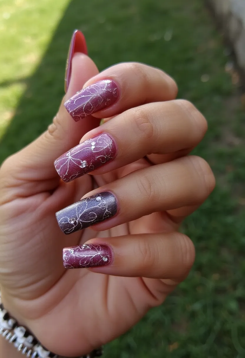 This nail design features a lovely gradient color palette of deep maroon transitioning into a shimmering silver. The nails are shaped in a medium-length squoval (square oval) form, which provides a balanced and elegant appearance. The intricate design includes delicate white floral patterns spiraling across each nail, embellished further with small, shimmering rhinestones that add a touch of sophistication and sparkle. Judging by the glossy and smooth finish, it appears that the treatment used is likely gel, known for providing a durable and high-shine result. The overall design exudes a sense of elegance and would be well-suited for special occasions or festive events, adding a refined touch to any ensemble.