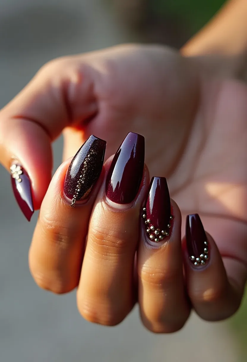 The nail design features a deep burgundy color palette with a glossy finish, indicative of a gel treatment due to the high shine and smooth, even coverage. The nails are shaped in a long, slightly rounded square form, offering a sophisticated look. Intricate decorations include small golden beads arranged in elegant patterns near the cuticles and along one side of each nail, adding a touch of glamour and refinement. Some nails also have a fine, sparkly accent along the bead lines, enhancing the luxurious appearance. The rich color and sparkling embellishments suggest this design could be suited for festive or formal events, possibly aligning with autumn or winter seasonal themes.