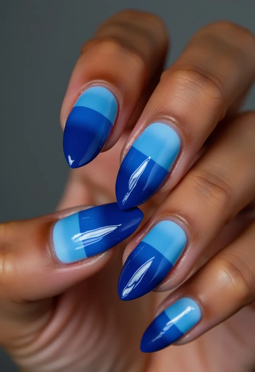 The nail design features a dual-toned color palette with shades of blue, specifically light blue and deep navy. The nails are almond-shaped, providing a sleek and elegant look. Each nail showcases an intricate pattern where the lower half is painted in light blue and the upper half in a solid deep navy, creating a modern and bold contrast. The nails appear to be treated with a gel polish, as evidenced by the high-gloss shine and smooth finish, ensuring durability and a polished appearance. This style would be ideal for winter season themes, as the cool blue tones evoke a crisp, frosty feel that is perfect for the colder months or for special occasions where a sophisticated and contemporary look is desired.