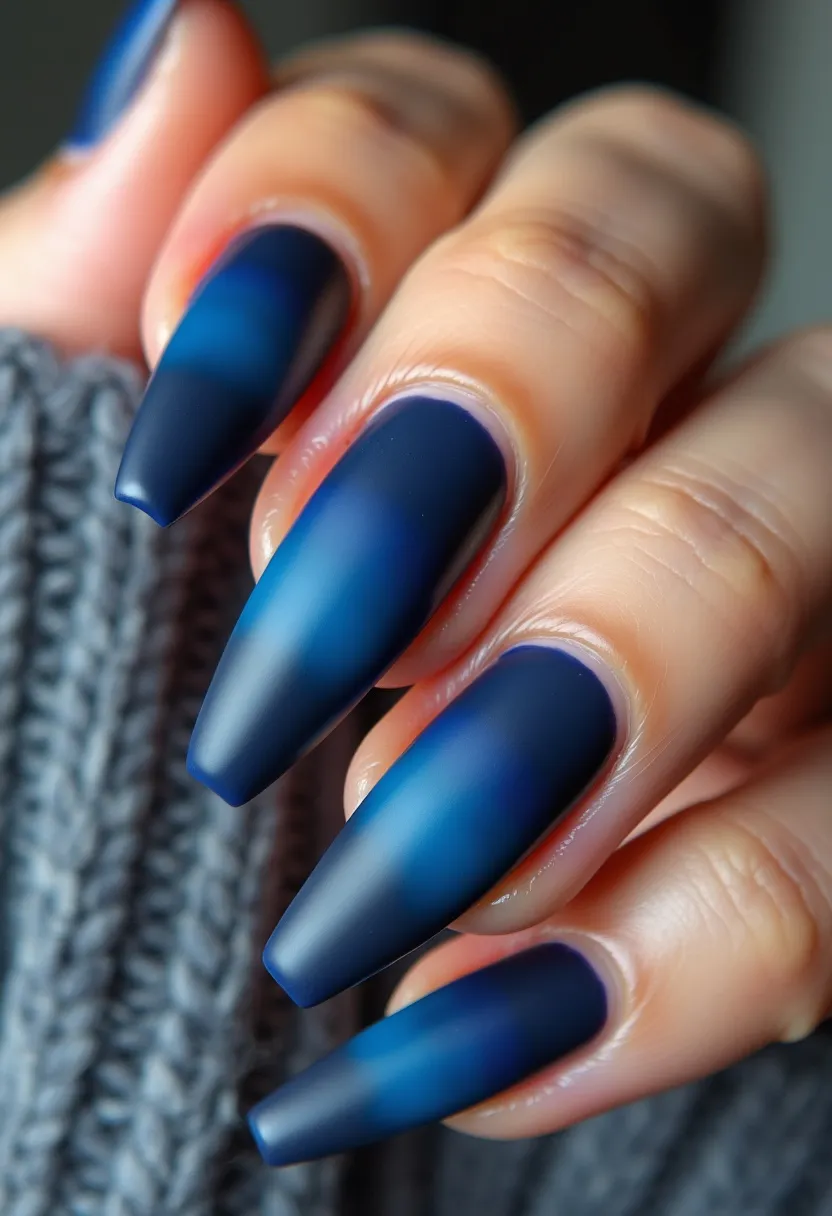 The nail design features an elegantly sculpted almond shape with a stunning gradient color palette transitioning from deep navy blue at the cuticle area to a slightly lighter hue towards the tips, giving a subtle ombre effect. The nails appear to have a matte finish, likely achieved through gel treatment, adding a sophisticated and sleek look. This design is free of additional patterns or decorations, relying on the smooth color gradient and matte texture to stand out. The overall aesthetic is modern and chic, suitable for any season or special occasion, emphasizing a minimalist yet striking appearance.