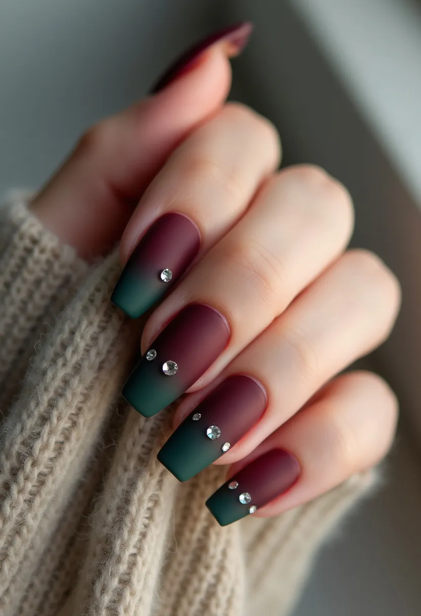 The nail design features a sophisticated color palette of burgundy and deep green with a beautifully blended ombre effect. The nails are shaped into a classic coffin style, providing an elegant and modern look. Adorning the nails are small, strategically placed rhinestones, adding a touch of sparkle and luxury to the overall design. The finish appears to be matte, which is often achieved using gel polish for its durability and smooth texture. This nail design could be ideal for the autumn or winter seasons due to its rich, darker hues and is suitable for special occasions or holiday events, where a more refined and festive appearance is desired.