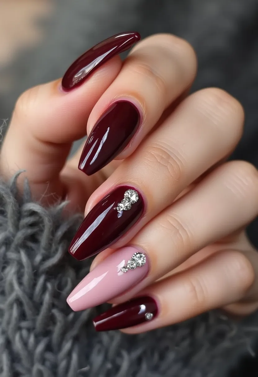 The nail design features an elegant and sophisticated color palette predominantly consisting of deep burgundy and a pale pink shade. The nails are shaped into a stiletto style, providing a sharp and elongated appearance. The design incorporates intricate decoration, with the middle and ring fingers adorned with sparkling rhinestones, adding a touch of glamour and sophistication. The treatment appears to be done using a gel polish, ensuring a glossy and durable finish. This nail design is versatile and could be suitable for special occasions such as formal events or festive celebrations, particularly during the winter or holiday season due to its rich and luxurious color scheme.