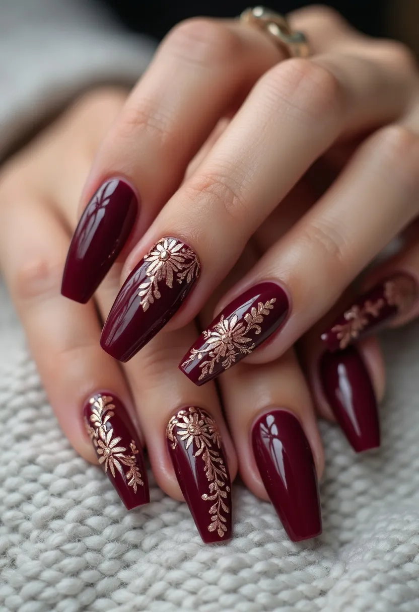 This nail design showcases a sophisticated color palette with a deep burgundy base that exudes elegance. The nails are shaped into a long, almond style, adding length and a sleek silhouette to the hands. Intricate gold floral patterns are delicately painted onto a few of the nails, creating a stunning contrast against the rich burgundy backdrop. The floral detailing appears to be meticulously crafted, displaying leaves and petals for an ornamental effect. The nails have a glossy finish that suggests a gel treatment, providing a long-lasting, high-shine appearance. This design could be suitable for a formal occasion or the autumn season, given its warm, luxurious tones and elegant patterns.