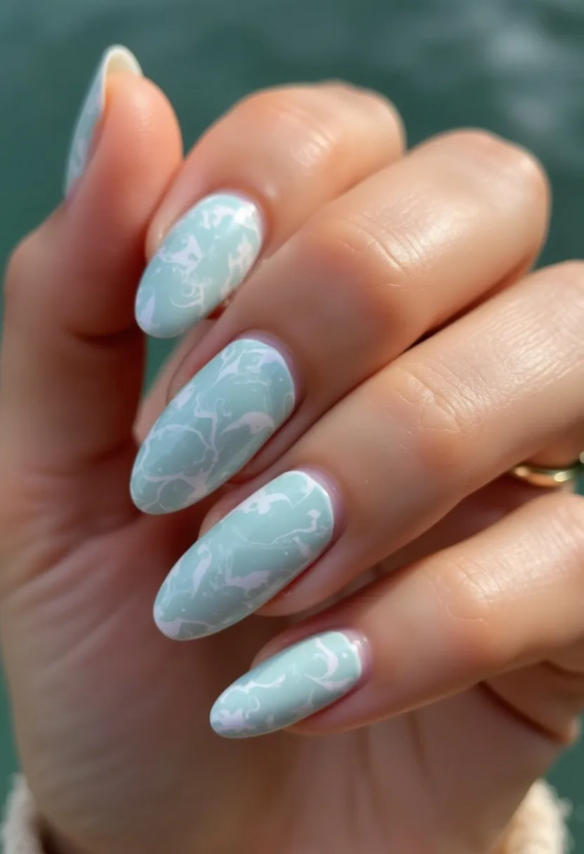 This nail design features a soft pastel mint green color palette with intricate white marbling patterns overlaying the nails. The nails are shaped in a stylish almond form, which elongates the fingers and adds an elegant touch. The pattern is consistent across all nails, indicating a water marble or marbling technique typically achievable with gel or acrylic treatments, giving the nails a smooth and glossy finish. This fresh and light color selection, along with the delicate marbling, suggests a design suitable for spring or summer seasons, or perhaps for a special occasion like a bridal shower or garden party. The overall look is sophisticated yet playful, showcasing meticulous craftsmanship in nail art.