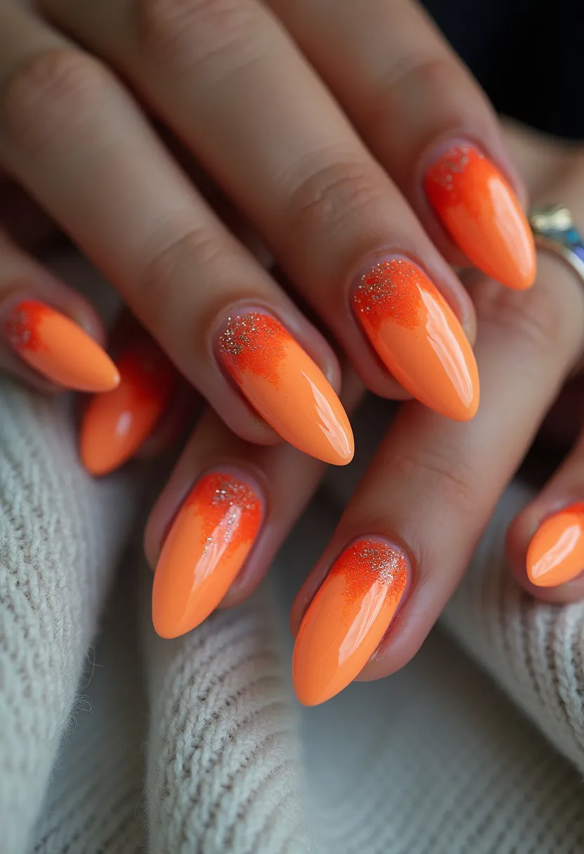 The nail design showcases a vibrant color palette dominated by shades of orange, transitioning from a deeper orange at the base to a lighter shade towards the tips. The nails are shaped in a long, almond style, providing an elegant and elongating effect on the fingers. Intricate patterns are present at the base of each nail, featuring a gradient effect embellished with fine glitter details, adding a touch of sparkle. The nail treatment appears to be gel, as evidenced by the high-gloss finish and smooth surface. The overall design has a lively and festive feel, making it suitable for the summer season or special occasions that call for bold, eye-catching nails.