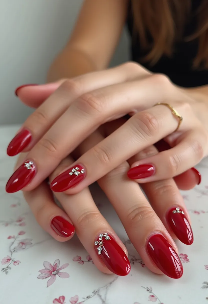 The nail design features a striking deep red color palette, exuding a classic and sophisticated appeal. The nails are crafted in an almond shape, providing an elegant and feminine look. Intricate decorations include small, glittering rhinestones arranged near the cuticles on several nails, forming delicate, floral-like designs that add a touch of glamour. These embellishments are likely set into gel polish, a popular choice for its durability and glossy finish. This design would be suitable for special occasions, such as weddings or holiday parties, due to its festive and refined aesthetic.