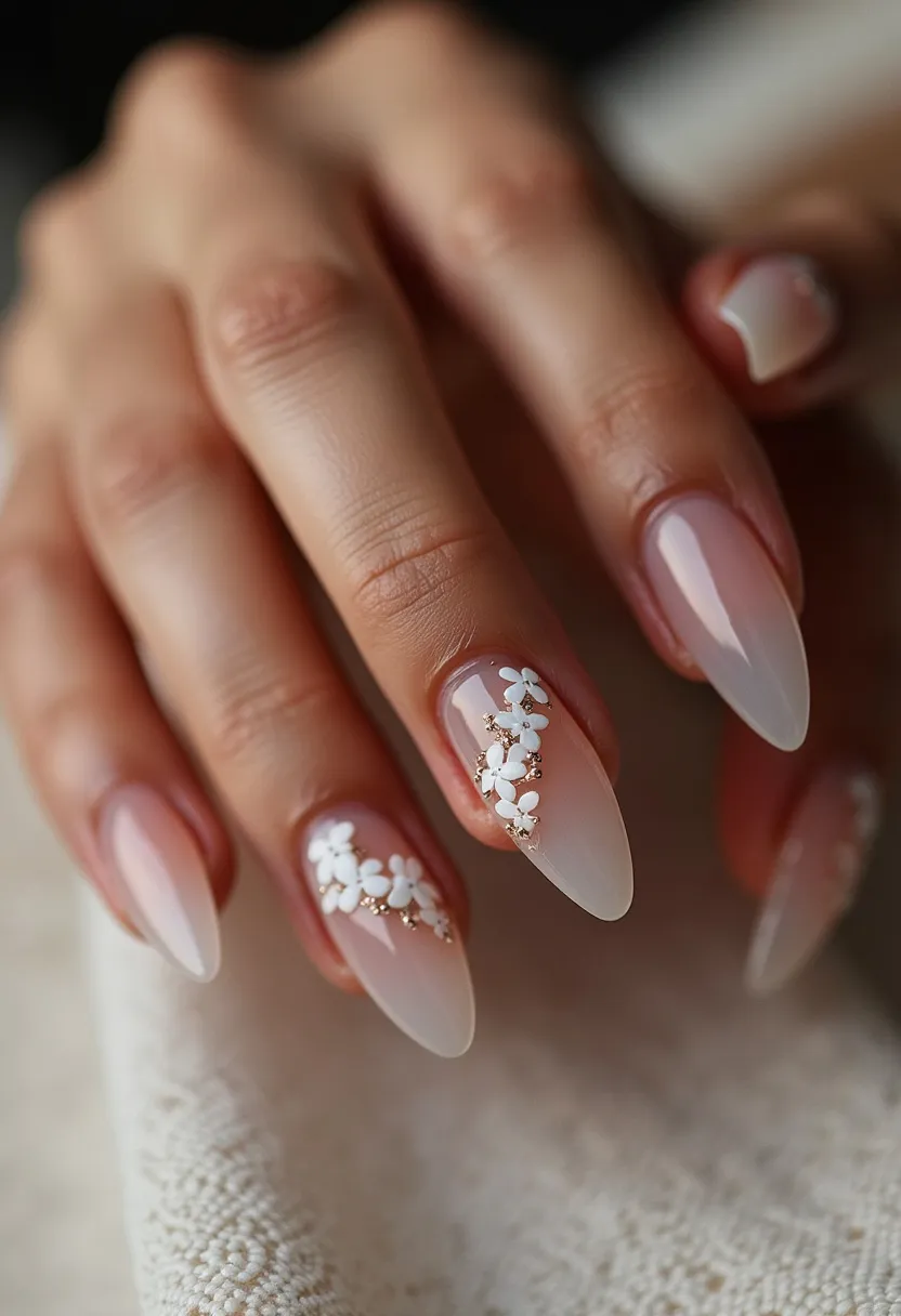 The nail design showcases a soft and elegant palette with a primary color of translucent, natural pink, complemented by white floral decorations. The nails are almond-shaped, providing a classic and sophisticated silhouette. Delicate 3D floral appliqués in white adorn a couple of nails, enhanced with subtle golden accents for added intricacy and charm. The finish appears smooth and glossy, indicating a gel treatment which helps to maintain the shine and durability of the design. This style has a fresh, spring-like theme, making it ideal for special occasions such as weddings, bridal showers, or other springtime events where elegance and delicacy are desired.