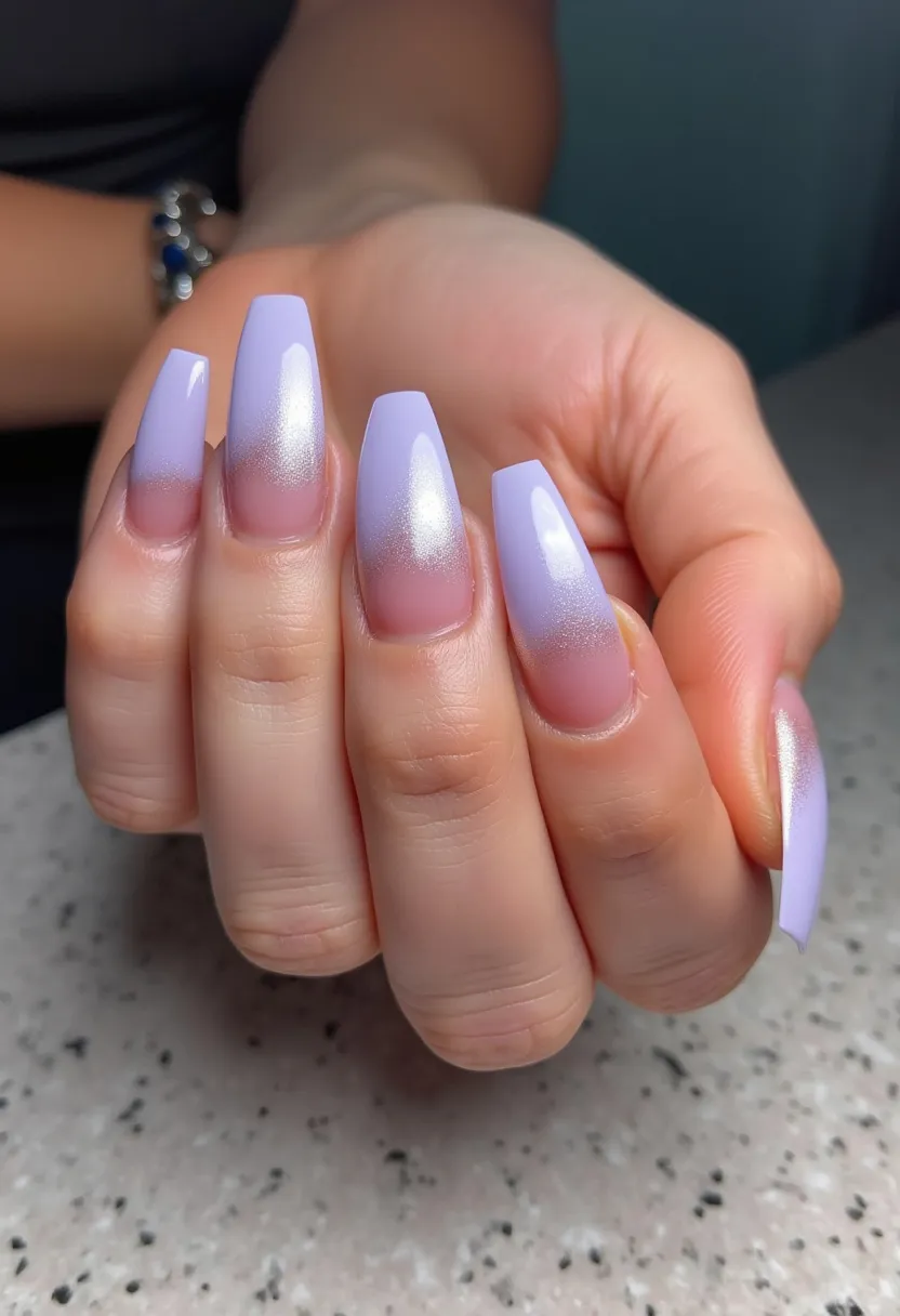 The nail design showcases a beautiful gradient effect featuring a subtle transition from a natural nude base to a soft, shimmering lavender tip. The nails are shaped into a long, square coffin-style, giving them an elegant and elongated appearance. The choice of color palette, dominated by pastel lavender with a touch of iridescent shimmer, lends a delicate and graceful aura. Although the type of nail treatment is not explicitly visible, the glossy finish suggests either gel or acrylic could be used. The overall design is both sophisticated and understated, making it suitable for various occasions, including springtime events or special gatherings. The gradient shimmer effect adds a unique touch, making these nails stand out with refined elegance.