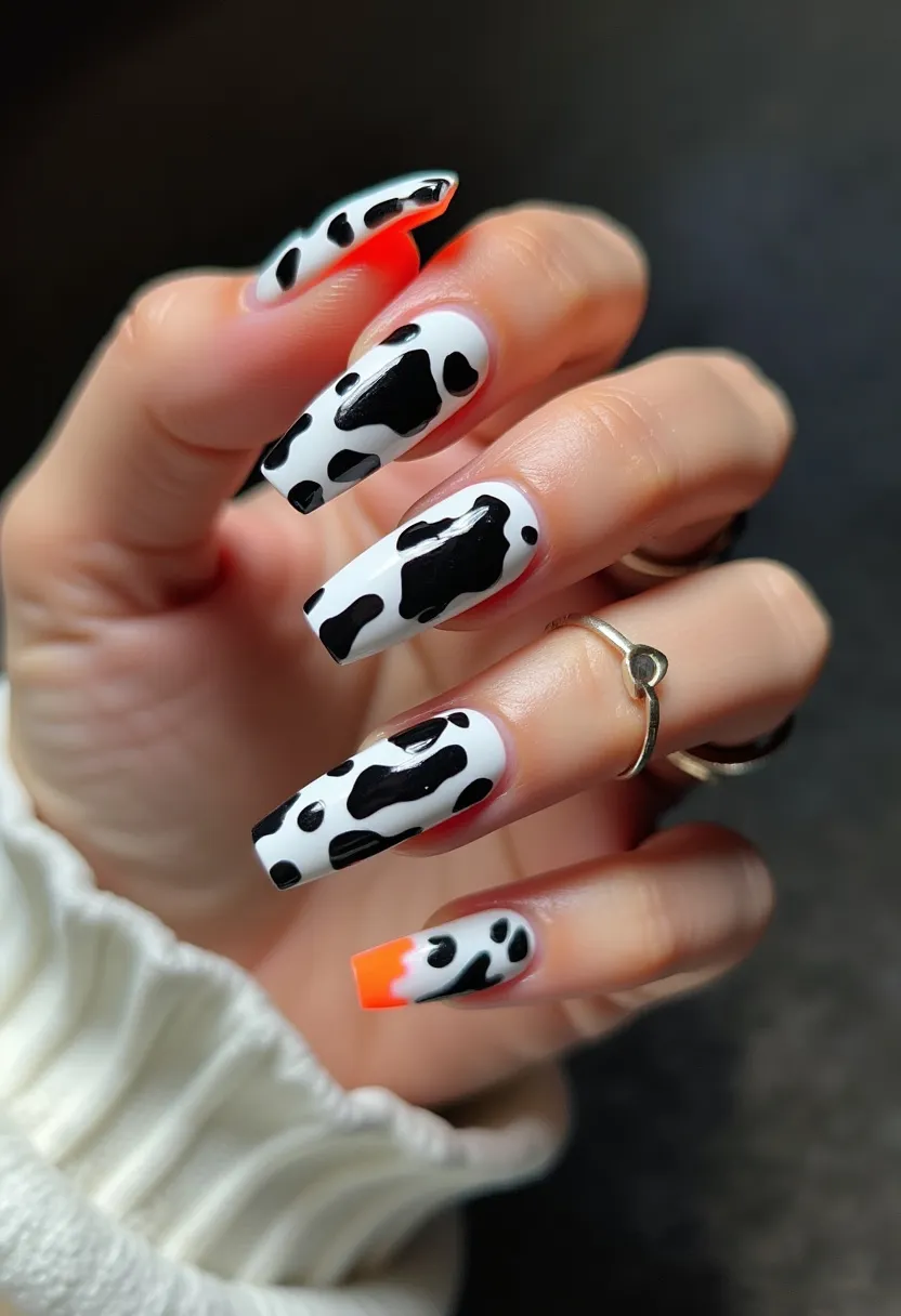 This nail design features a striking black and white color palette with a cow print pattern on each nail. The nails are shaped in a long square format. One distinct detail is the addition of a single bright orange tip on the ring finger, adding a pop of color to the monochrome design. The nails appear to be done using a gel treatment, which gives them a smooth and glossy finish. The cow print pattern, commonly associated with a playful and bold style, makes the nails vibrant and unique. There is no indication of a specific seasonal theme or special occasion for this nail design.