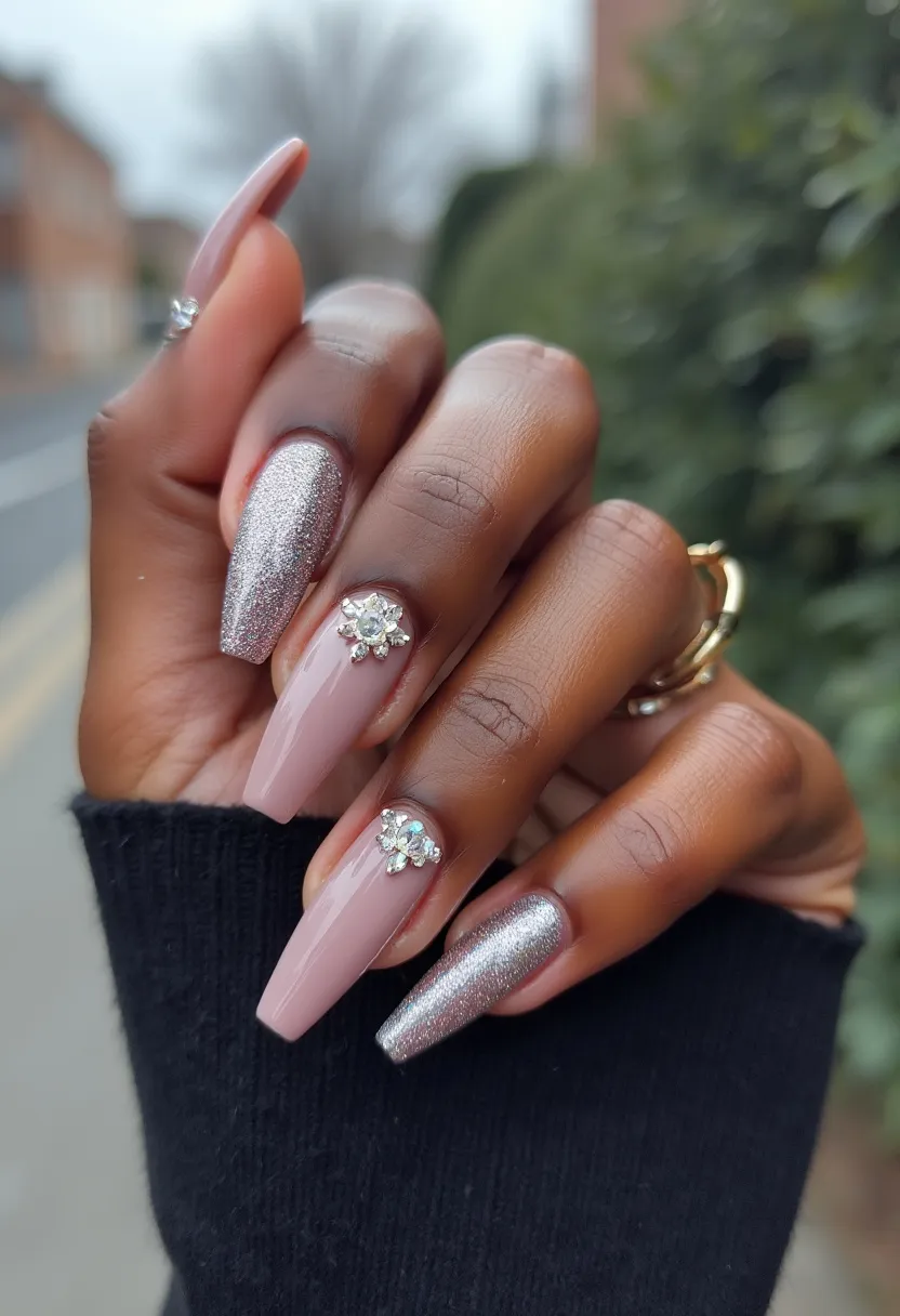 The nail design showcases a sophisticated color palette comprising a muted nude pink and a dazzling silver glitter. The nails are shaped in a long, elegant coffin form, enhancing the overall sleek appearance. Each hand features a combination of the nude pink base on most nails, while an accent nail is entirely painted in glittery silver on each hand. Additionally, a refined and intricate decoration is applied to two of the nude pink nails, with the addition of rhinestone embellishments forming floral shapes near the cuticle area. The nails seem to be treated with gel, giving them a high-gloss finish and long-lasting durability. This design exudes a festive and glamorous vibe, suitable for special occasions like weddings or holiday parties.