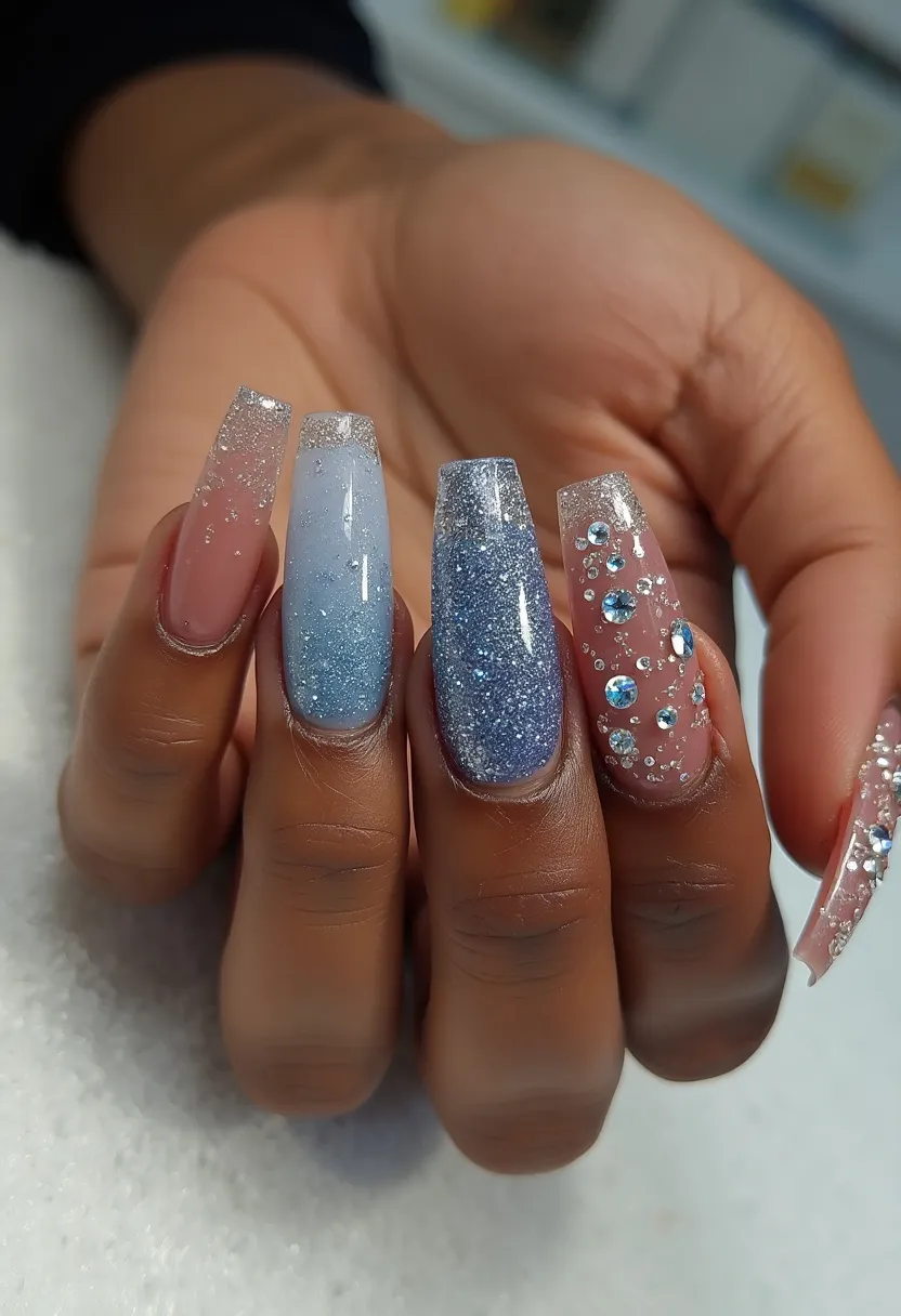 The nail design features a palette of cool blues and soft pinks, accented with silver glitter and rhinestones. The nails are shaped into long, tapered squares, creating an elegant and stylish look. Each nail varies in its design - one nail showcases a gradient effect from blue to clear with scattered glitter, another is fully coated in blue glitter, while others are adorned with pink polish and intricate patterns of rhinestones. This appears to be a gel nail treatment, offering a smooth and glossy finish. The glitter and rhinestones suggest a celebratory or winter-themed design, ideal for special occasions or festive events.