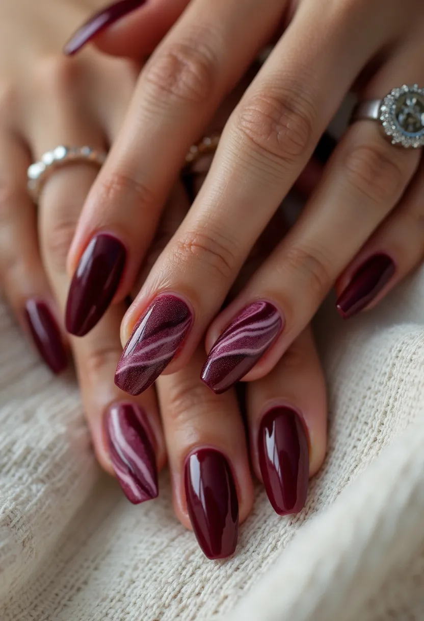 The nail design showcases an elegant and sophisticated look with a burgundy color palette. The nails are almond-shaped, providing a refined and elongated appearance to the hands. The primary color is a deep, glossy burgundy, which is complemented by intricate marbled patterns on a couple of accent nails. These marbled designs incorporate a lighter shade of burgundy with white swirls, adding a touch of artistry and depth to the overall design. The treatment appears to be a gel manicure, giving the nails a glossy and durable finish. This design is perfect for fall or winter seasons due to the richness of the color, and it could be suitable for formal occasions or festive events.