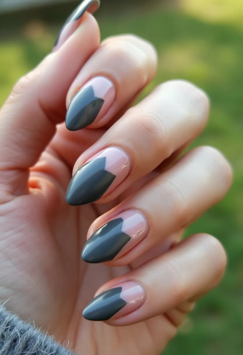 The nail design features almond-shaped nails showcasing a gray and nude pink color palette. Each nail is adorned with a geometric pattern consisting of a large gray chevron that sits prominently on the lighter pink base color, creating a striking yet sophisticated look. The finish appears glossy, indicating a gel or shellac treatment that enhances the durability and shine of the nails. This design is versatile and can be suitable for both everyday wear and special occasions, lending an air of modern elegance with a minimalistic aesthetic.