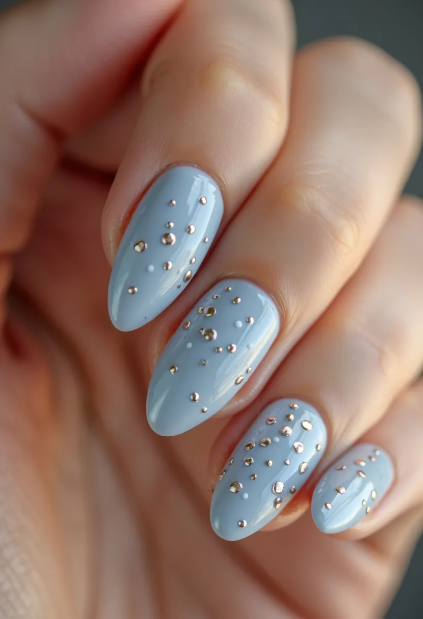 The nail design showcases a chic, modern aesthetic with an almond nail shape, which is both elegant and trendy. The color palette features a soft, pastel blue base, creating a serene and sophisticated look. Tiny metallic studs are meticulously placed across the nails, adding a touch of glamour and sparkle. This intricate pattern creates a dynamic contrast against the pale blue background. The nails appear to be treated with gel or shellac, ensuring a glossy and long-lasting finish. This design could be suitable for various occasions, from casual outings to more formal events, and the light blue hue hints at a possible spring or winter seasonal theme.