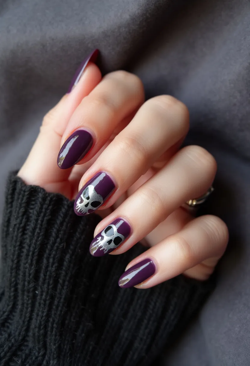 The nail design features a rich, deep purple color palette with an almond shape. The design includes intricate silver skull patterns on two nails, adding a striking and edgy element. The nails are likely treated with gel polish, given the high-gloss finish and smooth appearance. The silver skull decorations suggest a possible Halloween or gothic theme, perfect for seasonal events or special occasions that embrace a darker aesthetic. The combination of the dark purple base with the metallic skull designs creates a bold and dramatic look.