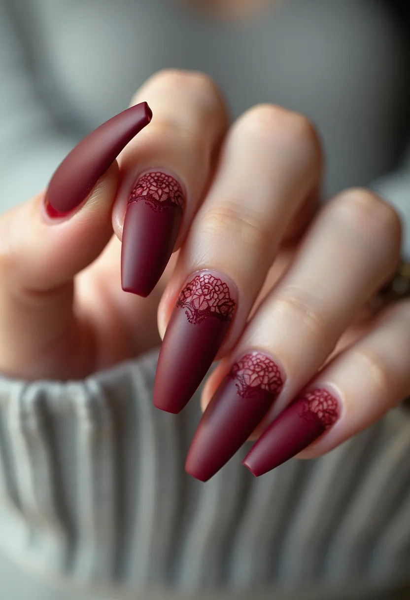 The nail design features a rich, deep burgundy color, with a matte finish, giving it an elegant and sophisticated look. The nails are shaped into a long coffin shape, which enhances the overall dramatic effect. Intricate lace-like patterns in a slightly darker shade are delicately painted near the cuticles, adding a touch of intricacy and femininity. This design likely utilizes acrylic or gel nail treatments for its durable, polished finish. The choices of colors and patterns would be fitting for a formal event or for seasonal themes like autumn or winter, where darker, warm tones are typically favored.