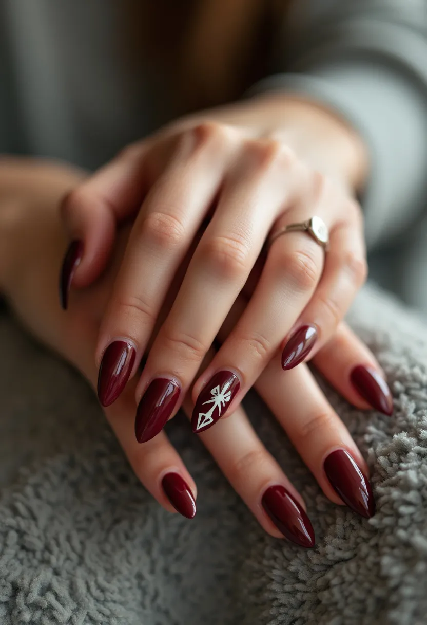 The nail design features an elegant palette with a rich, deep burgundy color that covers the entire surface of the nails. The nails are shaped in a sleek and elongated almond form, enhancing their sophisticated appearance. On the ring finger, a detailed white geometric pattern resembling an arrowhead or abstract design adds an intricate and artistic accent to the overall look. This design appears to utilize gel polish, given the glossy and smooth finish. The deep burgundy color and subtle white design could associate this nail art with a winter or holiday theme, making it suitable for special occasions during this season.