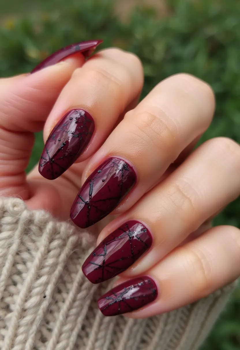 The  nail  design  features  a  burgundy  or  maroon  color  palette,  with  a  unique  pattern  of  cracks  or  lines  on  the  nails.  The  nails  are  shaped  in  a  natural,  oval  shape.  The  nail  treatment  appears  to  be  a  gel  or  acrylic,  as  it  is  well-defined  and  has  a  smooth  finish.