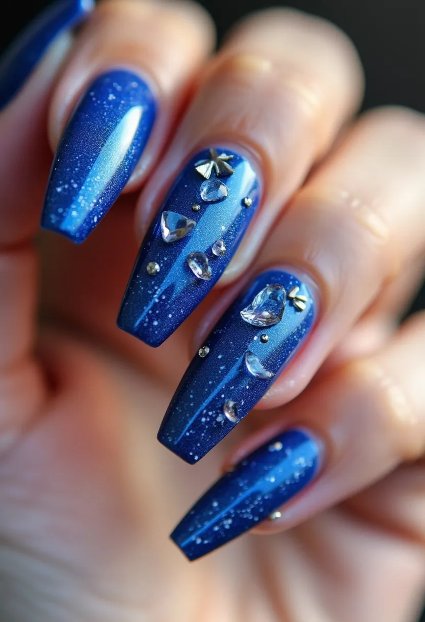 The nail design showcases a striking blue color palette with a gradient effect, blending from a deep navy at the base to a lighter blue towards the tips, adorned with specks of glitter that evoke a starry night sky. The nails are sculpted into a long coffin shape, offering an elegant and elongated appearance. Intricate patterns are formed by strategically placed rhinestones and small metallic studs, creating a three-dimensional look with a mix of clear and silver-toned embellishments that add a touch of luxury and sophistication. The smooth and glossy finish suggests the use of gel or shellac treatment, providing a durable and high-shine coating. This design exudes a winter or celestial theme, perfect for special occasions or festive events, where the sparkling elements highlight the celebratory spirit.