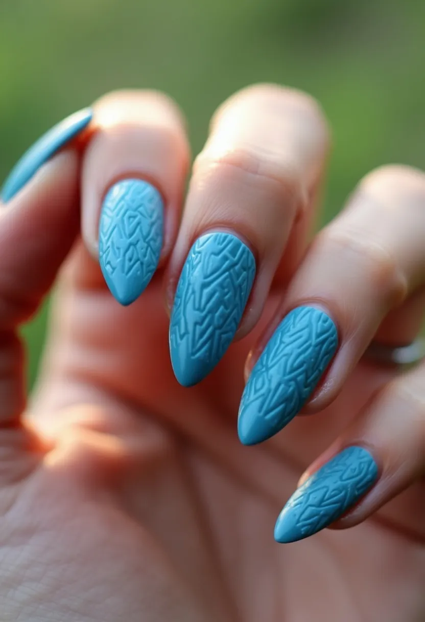 This nail design features a soft blue color palette, applied in what appears to be a gel or shellac treatment due to the smooth and glossy finish. The nails are shaped into a stiletto style, tapering to a rounded point. Intricate embossed patterns with geometric motifs adorn each nail, adding a three-dimensional texture to the design. This eye-catching and sophisticated style is versatile but may particularly suit the spring season or be appropriate for a special event, exuding a sense of elegance and meticulous artistry.