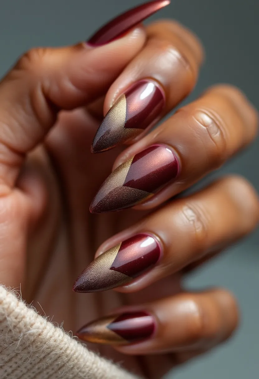 The nail design features a rich and sophisticated color palette dominated by burgundy and gold shades. The nails are long with a pointed stiletto shape, adding a dramatic flair to the overall look. The design includes an intricate geometric pattern, with a gold metallic accent forming a sharp, elegant contrast against the burgundy base, creating a visually striking V-shape near the tips. This is likely a gel treatment, given the glossy, smooth finish and the intricate detailing involved. The nail art hints at an autumn or festive season theme, with its warm, luxurious colors and sophisticated design, making it suitable for special occasions or holiday celebrations.