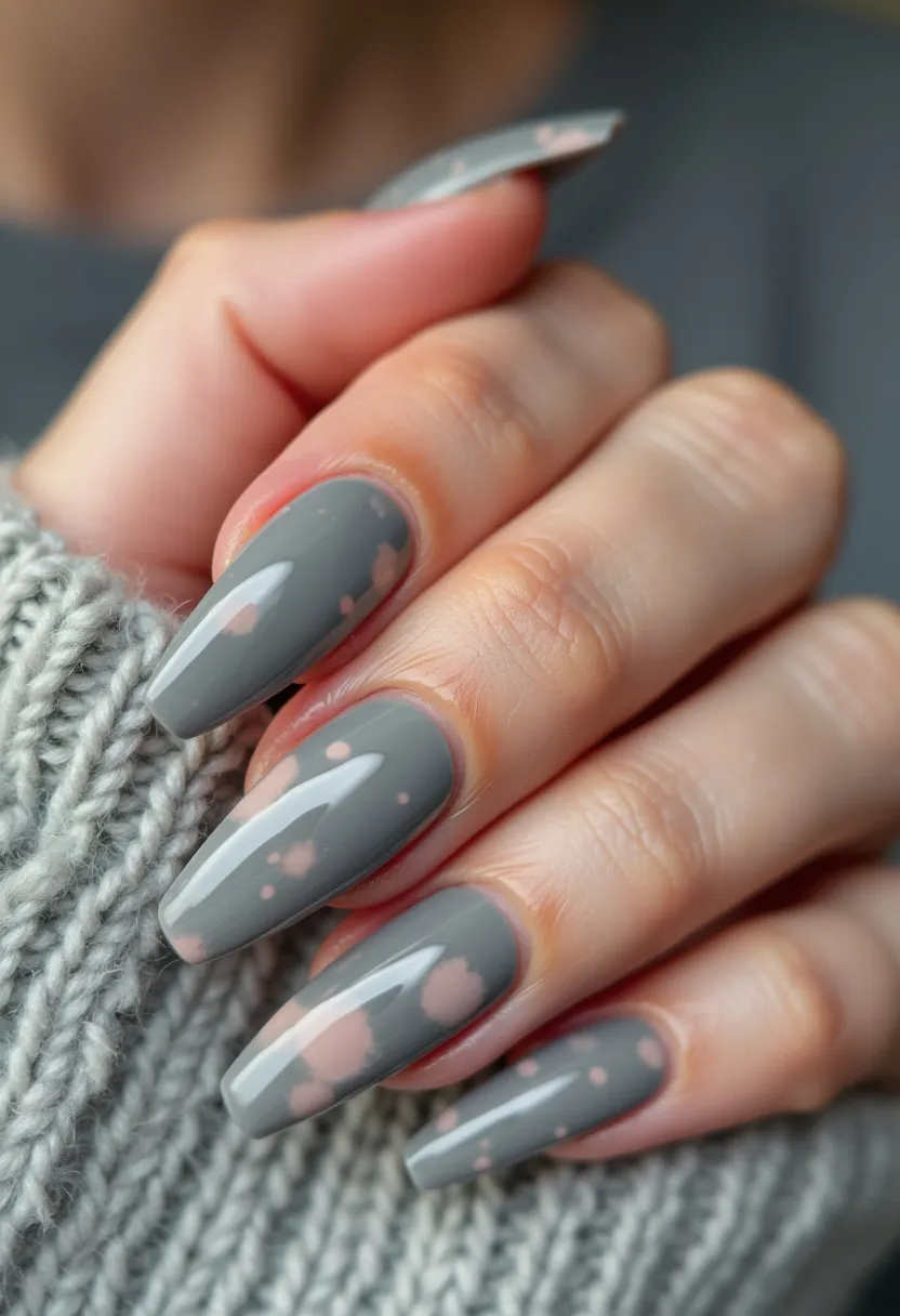 The nail design features a combination of muted grey as the primary color with light pink spots scattered across the surface, creating a subtle, marbled effect. The nails are long and shaped into a tapered, coffin style, providing a sophisticated and stylish look. The finish appears glossy, indicating a gel nail treatment that enhances durability and shine. This design, characterized by its understated elegance and contemporary vibe, makes it suitable for a winter or autumn season, potentially appealing for both casual wear and formal occasions. The intricate pastel pattern adds a unique touch to the overall aesthetic, setting it apart from plain monochromatic designs.