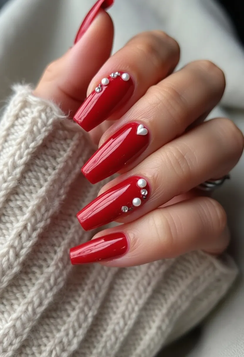 The nail design features a striking red color palette, which is bold and eye-catching. The nails are shaped in a long, coffin style, providing ample canvas for intricate decorations. The design incorporates small white pearls and crystals meticulously placed near the cuticles, adding a touch of elegance and sophistication. Additionally, a tiny white heart decoration is featured on one of the nails, accentuating the overall design with a subtle yet charming detail. The glossy finish suggests the use of gel nail treatment, which enhances durability and shine. This nail design could be suited for special occasions or festive celebrations, with its vibrant color and decorative elements offering a festive and luxurious feel.