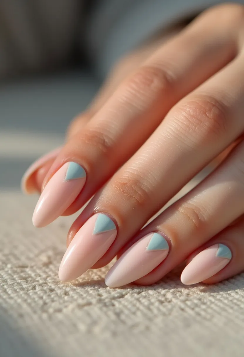 The nail design features almond-shaped nails painted with a soft, pastel pink base color. Each nail is adorned with a light blue triangular decoration at the cuticle area, adding a minimalist yet elegant touch to the overall look. The intricate pattern of the triangle creates a subtle but eye-catching contrast against the pink background. The nails are treated with a gel polish, giving them a glossy and smooth finish that enhances their durability and shine. This design, with its pastel palette and delicate details, is versatile and could be suitable for spring or summer seasons, or for occasions that call for a refined and sophisticated appearance, such as weddings or formal events.