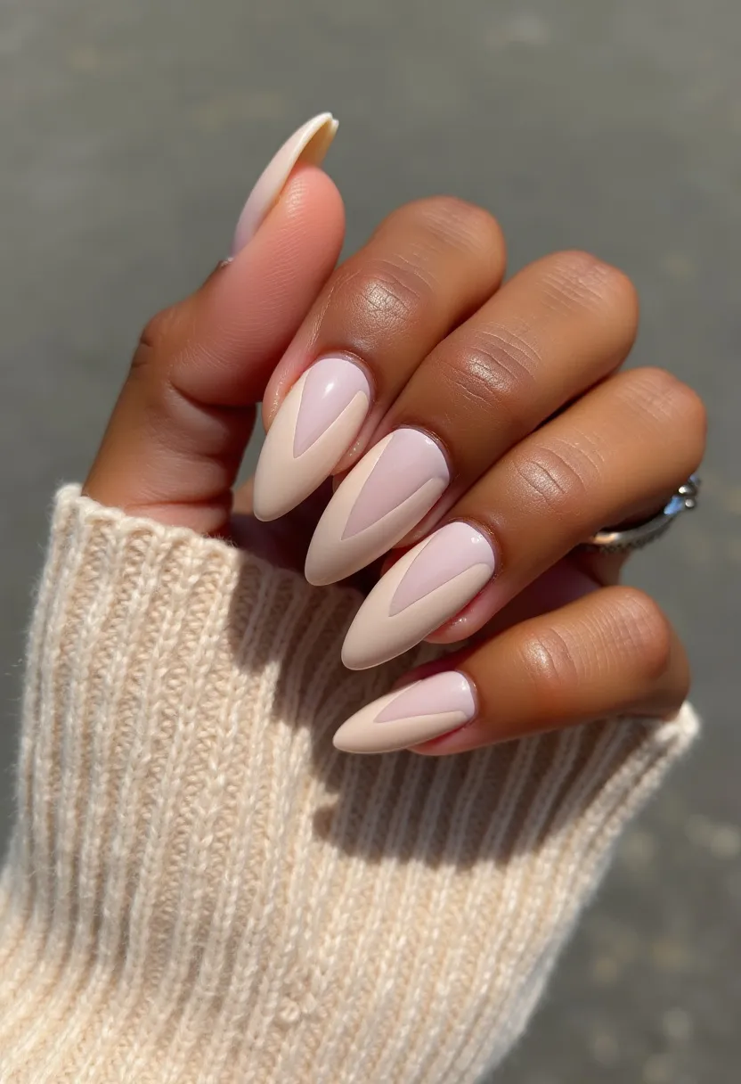 The nail design features almond-shaped nails painted with a contemporary and elegant palette of soft pastel pink and nude beige. Each nail showcases an intricate geometric pattern with a reverse chevron or arrowhead design, where the tips are highlighted in the nude beige shade, creating a striking contrast against the soft pink base. This design is likely achieved with gel or shellac treatment, given the high-gloss finish and durability typical for such meticulous work. The minimalist yet chic pattern makes this design versatile for various occasions, from upscale social events to everyday sophistication, offering a subtle yet stylish nod to modern nail art trends.