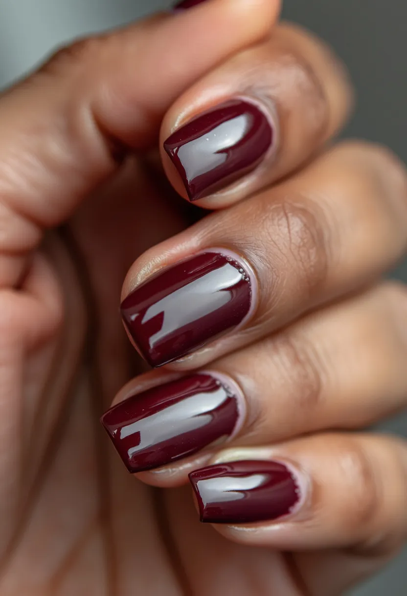 The nail design features a rich, burgundy color palette, giving off a sophisticated and elegant vibe. The nails are shaped in a short square style, providing a neat and clean appearance. The nail treatment appears to be a glossy gel, evident from the high-shine finish that reflects light beautifully. There are no intricate patterns or additional decorations, emphasizing the simplicity and classic style of the design. This nail look is versatile and suitable for various seasonal themes or special occasions, particularly for autumn or formal events, given its deep and warm color tone.