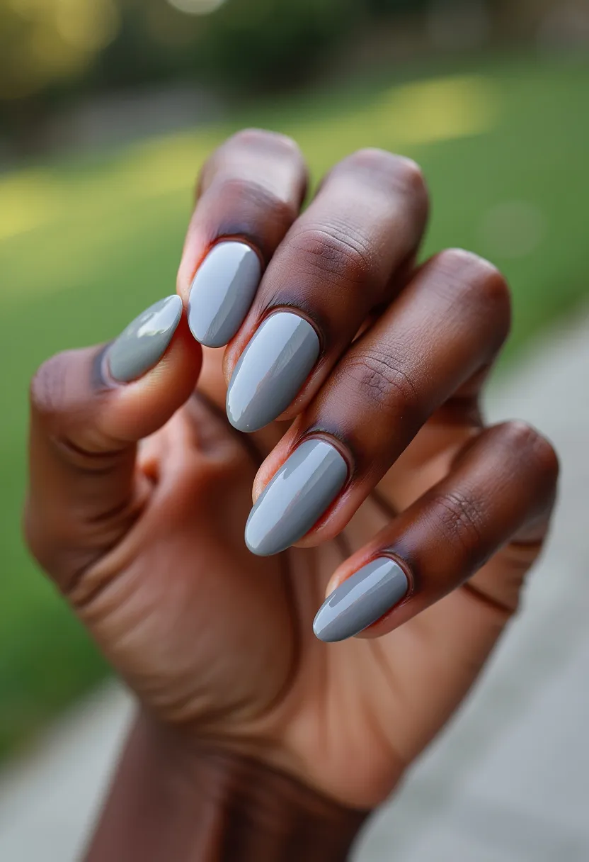 The nail design showcases a sleek and sophisticated look with a monochromatic color palette of slate grey. The nails are shaped in a modern almond style, adding a refined and elegant touch to the overall appearance. The finish is exceptionally glossy, suggesting a gel or shellac treatment, which provides a durable and shiny surface. There are no additional intricate patterns or decorations, keeping the design minimalistic and versatile for various occasions. The neutral grey hue and straightforward design make it suitable for both professional settings and everyday wear, with a chic and understated aesthetic.