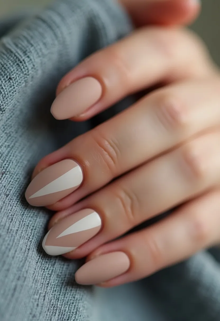 The nail design features a sophisticated color palette primarily in nude and soft beige tones. The nails are almond-shaped, providing a sleek and elegant appearance. Highlighting the design are intricate geometric patterns on a couple of the nails, with a white, elongated triangular shape adding a striking contrast to the neutral background. The smooth, glossy finish of the nails suggests the use of gel treatment, which enhances their durability and shine. This minimalist yet stylish design is versatile and suitable for various occasions, from casual outings to formal events, and could easily complement a wide range of outfits across different seasons.