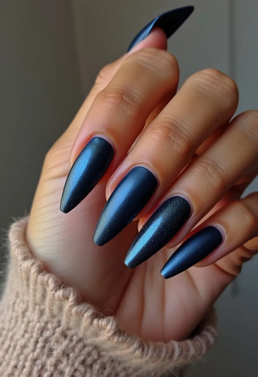 The nail design features a sleek and elegant look with a deep, shimmering navy blue color palette. The nails are sculpted into a stiletto shape, characterized by their long, pointed tips, adding a dramatic flair. The matte finish with a subtle sheen suggests that the treatment is likely gel or acrylic, known for their durability and glossy finish. There are no additional intricate patterns or decorations, keeping the design clean and sophisticated. This style could be ideal for a winter season or a formal evening event, with its dark, cool tones and polished appearance.