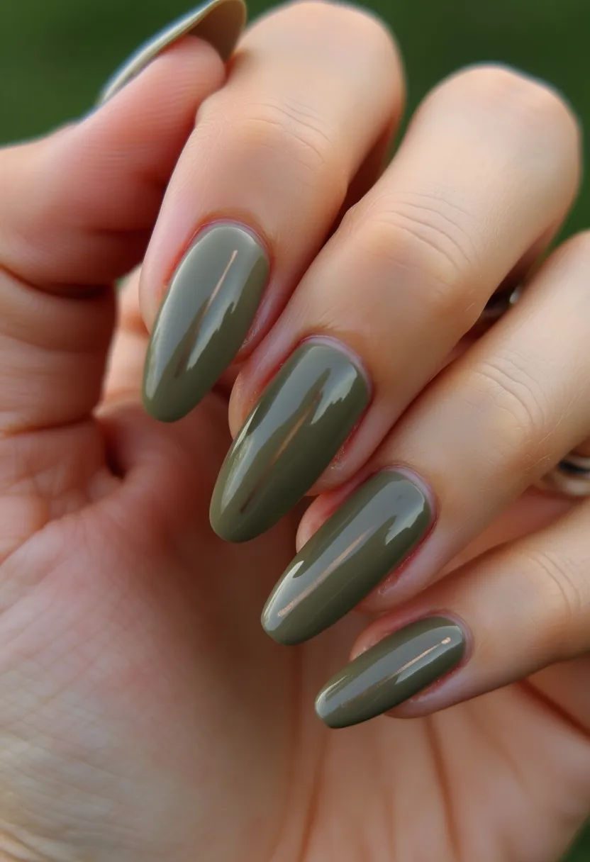 The nails feature a polished, olive green color palette, characterized by a glossy finish that suggests a gel or shellac treatment. Shaped with an almond profile, the nails exhibit a smooth curvature that elongates the fingertips elegantly. The design is kept simplistic and sophisticated with a solid monochromatic green hue, free from intricate patterns or additional decorations. The earthy green tone is reminiscent of a fall or autumn theme, making it suitable for the season's natural color scheme. The overall look is clean and polished, perfect for a chic and minimalist aesthetic.