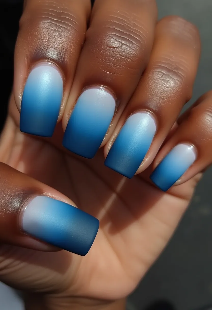 The nails feature a beautiful ombre design transitioning from a soft, light blue at the base to a rich, darker blue at the tips. The nail shape is square, creating a modern and clean aesthetic. This design is likely achieved with gel polish, given the smooth gradient effect and the distinct matte finish. The overall look does not include any additional intricate patterns or decorations, allowing the gradient itself to be the focal point. This minimalist yet elegant manicure would be particularly fitting for winter seasons or any formal occasion requiring a touch of sophistication.