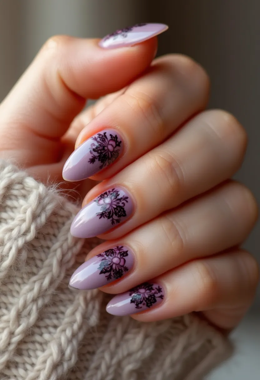 The nails in the design are almond-shaped and painted with a soft lavender base color. Each nail features an intricate floral pattern in black, giving a delicate and sophisticated appearance. The design appears to be done with gel polish, given the smooth finish and glossy sheen. The floral accents add a touch of elegance, suitable for various occasions, possibly aligning with a winter or fall theme due to the darker color palette in the patterns. The combination of the pastel base and intricate detailing makes this nail design both timeless and stylish.