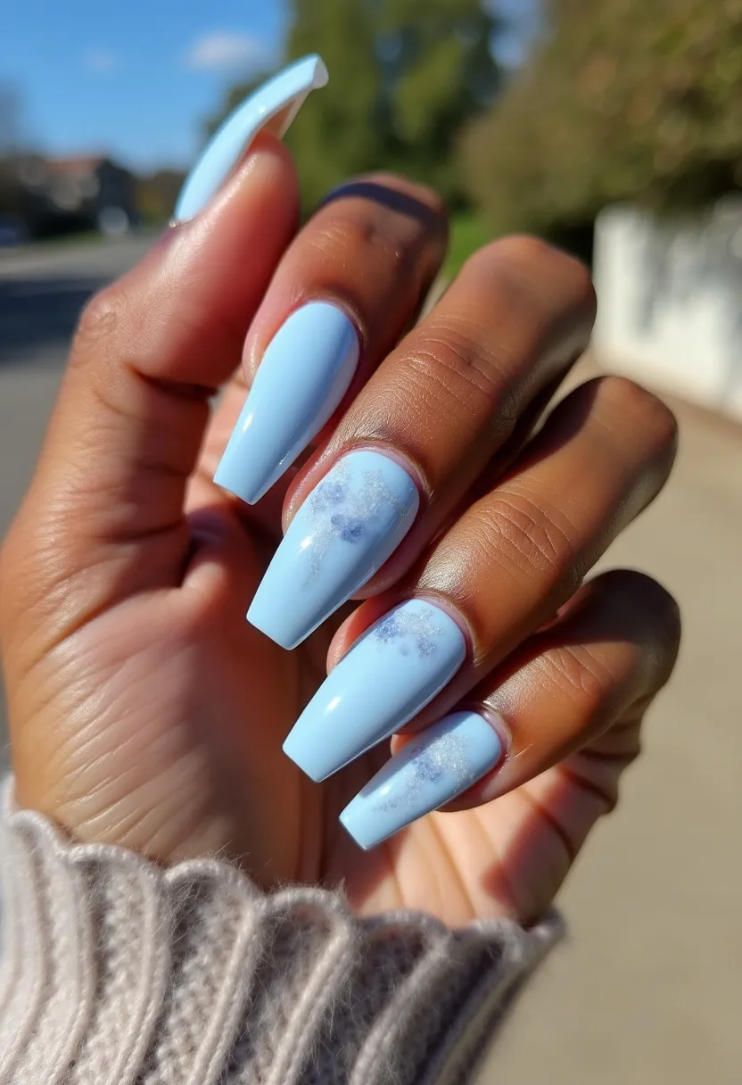 The nail design features long, coffin-shaped nails primarily painted in a delicate baby blue color. The middle and ring fingers have a subtle, intricate marble-like pattern in a slightly darker blue hue, adding a touch of elegance and texture to the overall look. The nails appear to be coated with a gel treatment, providing a glossy and smooth finish. This design has a soft and airy feel, making it suitable for a spring or winter theme, evoking a sense of coolness and serenity. The light blue palette and polished surface make this manicure perfect for both everyday wear and special occasions.