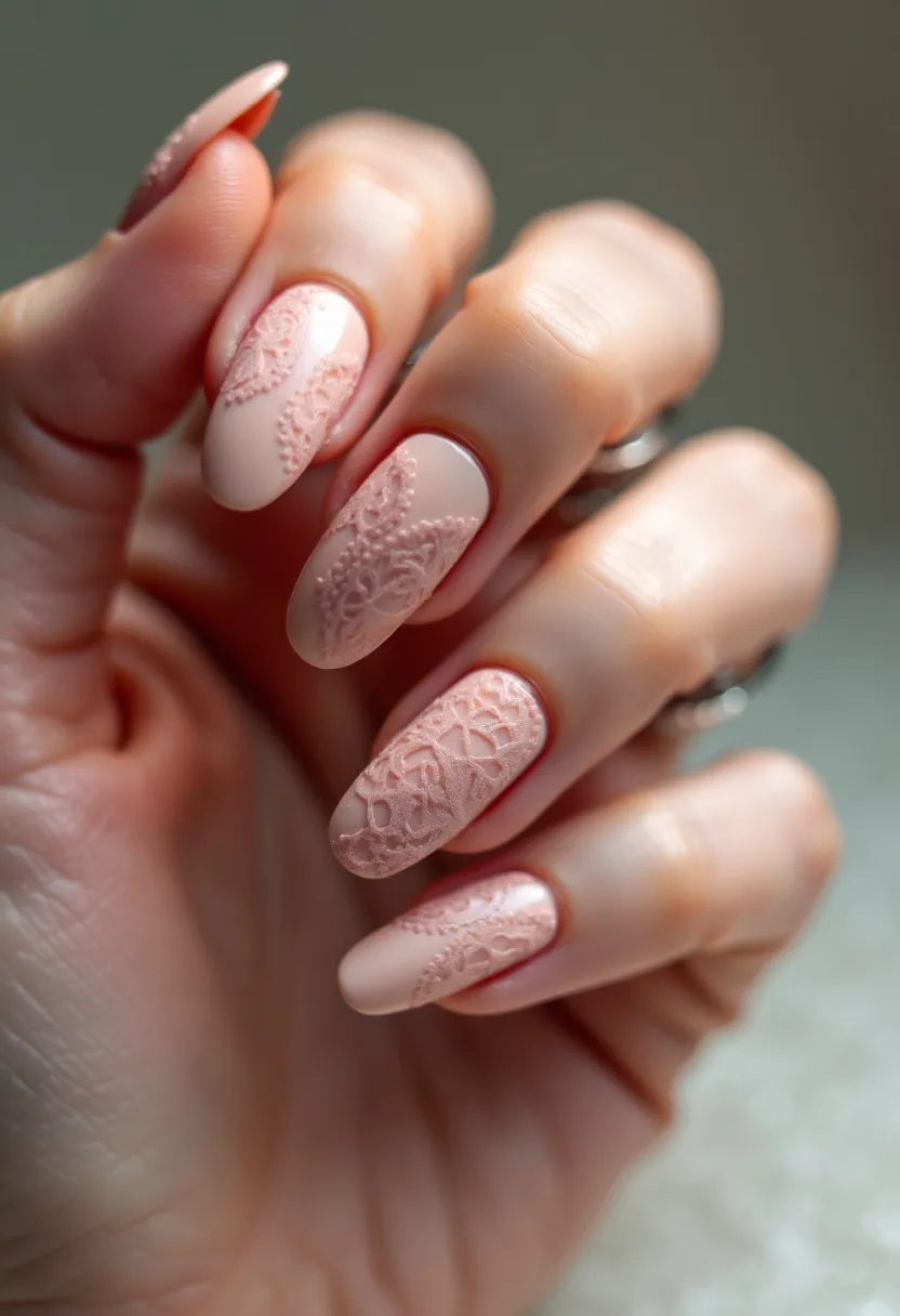 The nail design features a soft, nude pink color palette that gives the nails an elegant and sophisticated appearance. The nails are shaped in an almond style, which further adds to the delicate and refined look. Intricate lace-like patterns are embossed onto the nails, adding a textured, three-dimensional effect that is both subtle and intricate. This design likely utilizes a gel treatment to achieve the smooth and lasting finish, allowing for the fine details to be carefully crafted. The overall aesthetic of the nails suggests a theme that is ideal for romantic occasions or perhaps a bridal theme, given the lace pattern and gentle color choice.