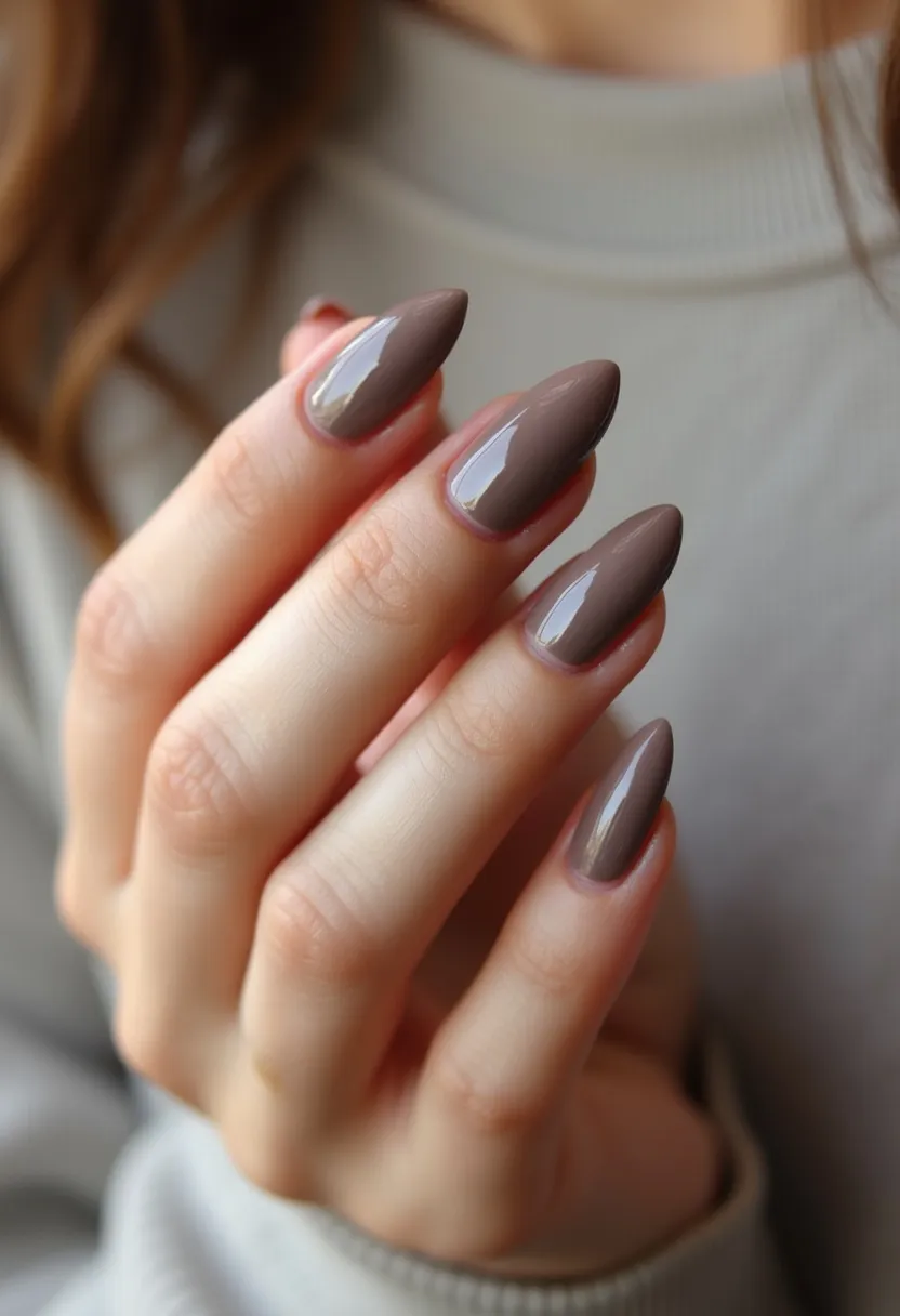 The nails in the design feature an almond shape and are coated with a single tone of glossy taupe polish, reflecting a subtly sophisticated look. The application appears smooth and thick, suggesting a gel or shellac treatment known for its durability and shine. The absence of intricate patterns or additional decorations keeps the design minimalistic yet elegant, suitable for both everyday wear and special occasions. The earthy taupe color lends itself well to an autumnal palette, making it a fitting choice for the fall season.