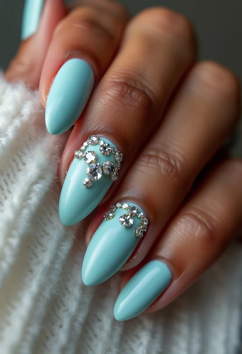 This nail design features a striking, glossy pale turquoise color palette. The nails are shaped into a sharp almond form, giving a sleek and elegant appearance. The design is accentuated with intricate silver and clear rhinestone decorations on the ring and middle fingers, forming a delicate, glittering pattern near the base of the nails. This embellishment adds a sophisticated and luxurious touch to the overall design. The nails appear to be treated with gel, providing a smooth and polished finish. The overall look is suitable for a special occasion or seasonal celebration, with a wintery, glamorous vibe due to the subtle yet eye-catching rhinestone accents.