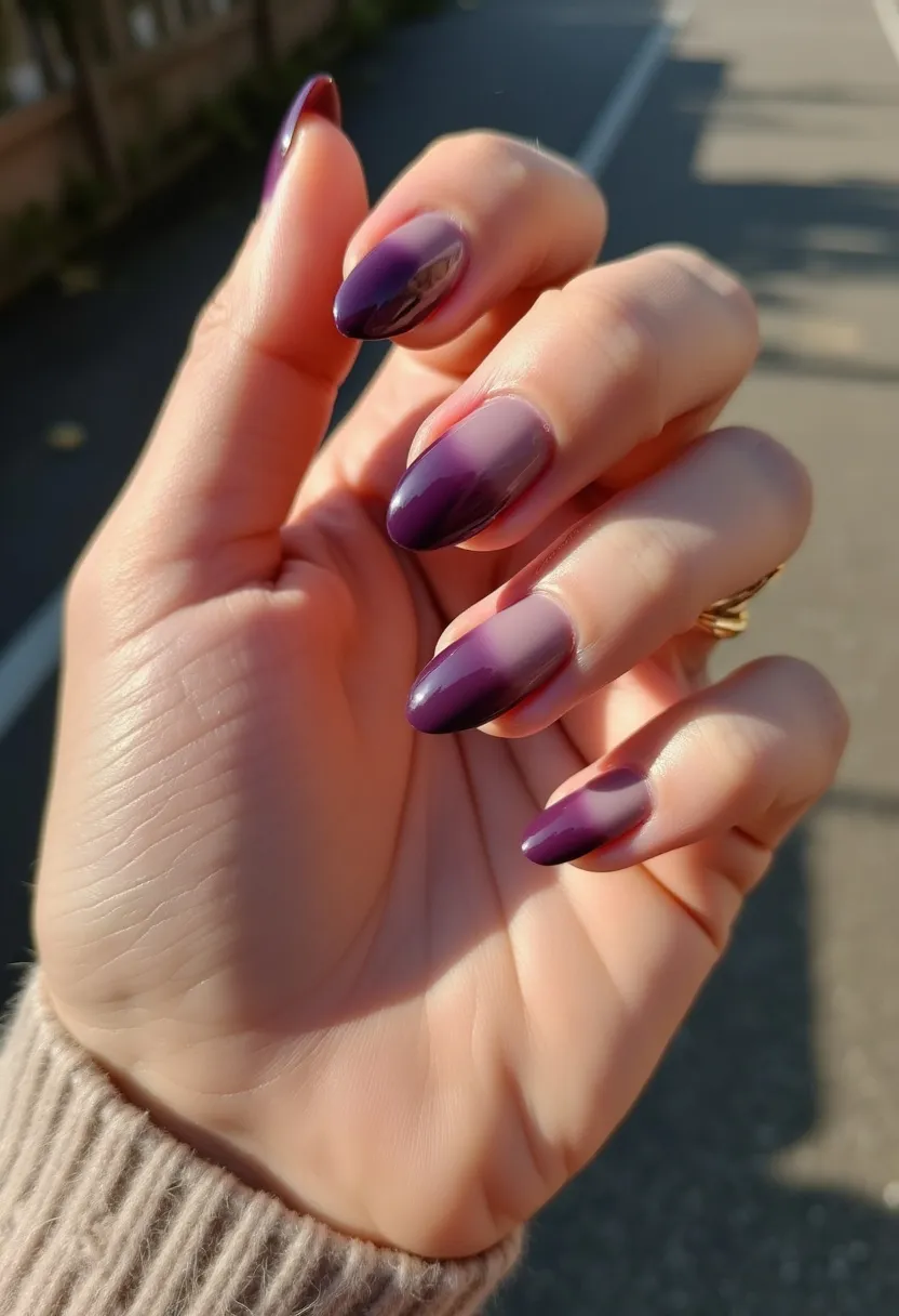 The nail design presented features an elegant gradient color palette transitioning from a deep, rich purple at the tips to a softer, more muted purple towards the base of the nails. The nails are almond-shaped, offering a sophisticated and elongated look. The gradient effect is meticulously blended, providing a smooth transition between the two shades of purple. This intricate design suggests a gel or acrylic nail treatment, known for its durability and glossy finish. The overall theme is versatile enough for various occasions, from everyday wear to special events, with a subtle nod to the cooler autumn or winter seasons due to the deeper color tones. The nails are finished with a high-shine clear topcoat, enhancing the depth and vibrancy of the colors.