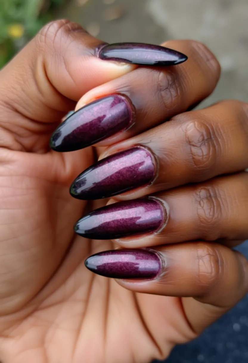 The nail design showcases a deep, rich, and glossy burgundy color palette with a slight shimmer effect. The nails are shaped in a long stiletto form, characterized by their pointed tips and tapered sides. The finish appears smooth and highly reflective, indicating a gel or shellac treatment that gives a durable, lustrous appearance. This sophisticated look is ideal for autumn or winter seasons, adding an elegant touch to festive or formal occasions. The lack of additional patterns or decorations highlights the classic and refined essence of the manicure.