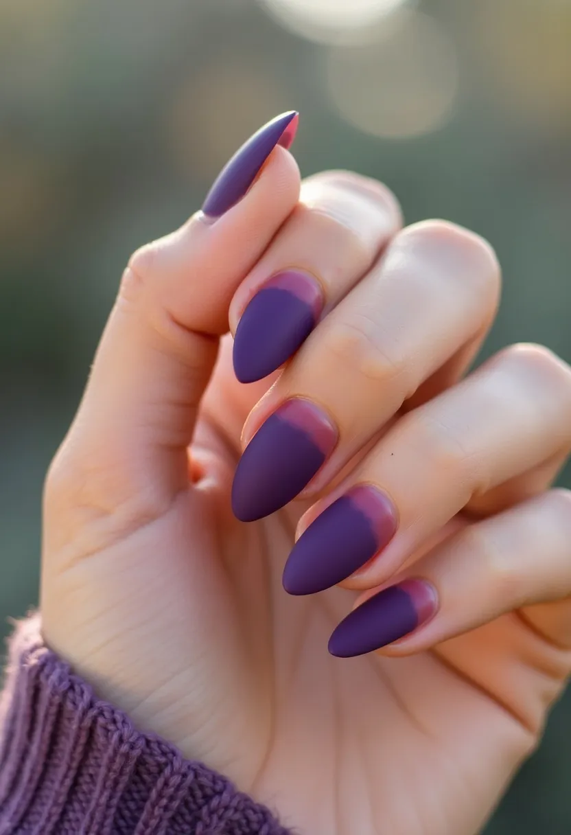 The nail design features a matte purple color palette with a gradient transitioning to a pink hue near the base of each nail, creating a subtle ombre effect. The nails are almond-shaped, offering a sleek and elegant look. The treatment appears to be gel, given the smooth and even application of color with a semi-translucent, glassy finish at the base, which characterizes gel nails. There are no intricate patterns or additional decorations, maintaining a minimalist style. This design could be suitable for seasonal themes like fall due to the rich purple tones, or for special occasions where a sophisticated yet simple nail design is desired.